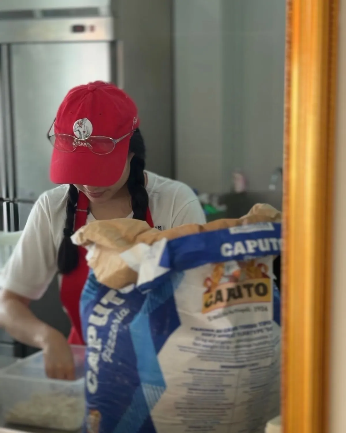 Nova reflected in a gilt mirror as she works, a sack of Caputo pizzeria flour open beside her