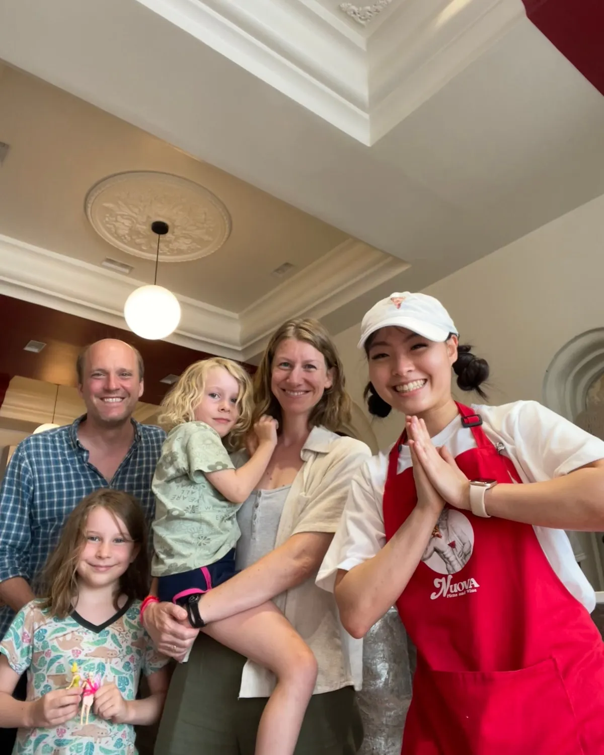 Nova greeting a family of four in the dining room with her hands together in a wai