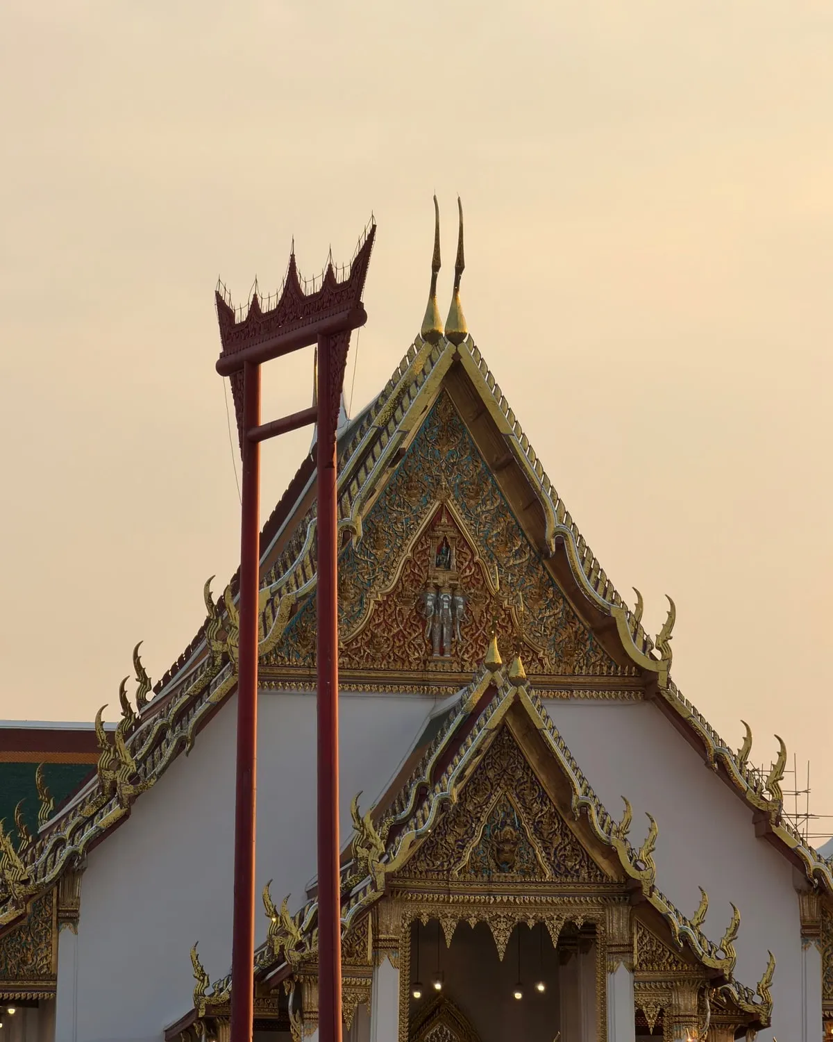 The Giant Swing standing against the gilded gable of Wat Suthat at dusk