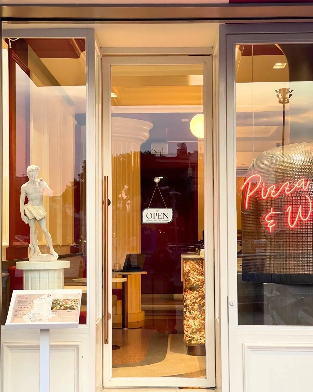 The Nuova doorway standing open at dusk, the David replica on a plinth beside it, an open sign and the Pizza and Wine neon glowing inside