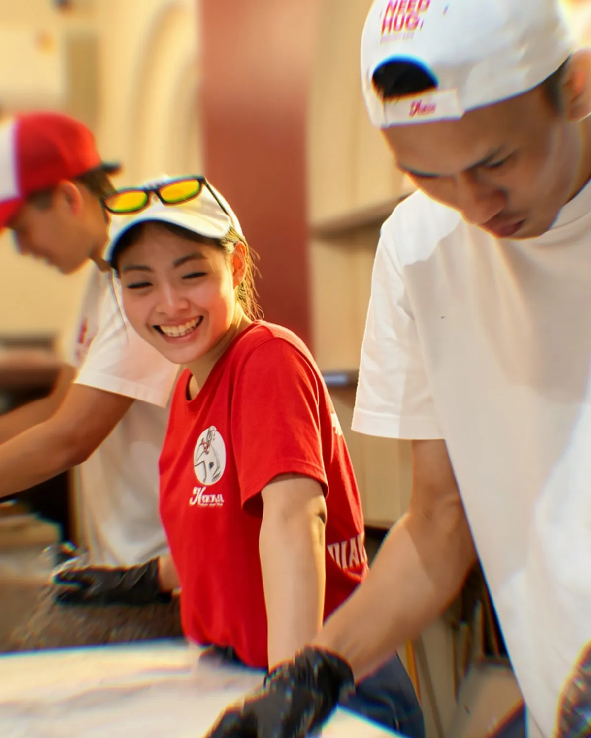 Nova and two of the kitchen team laughing over a pizza on the floured bench, all in Nuova caps
