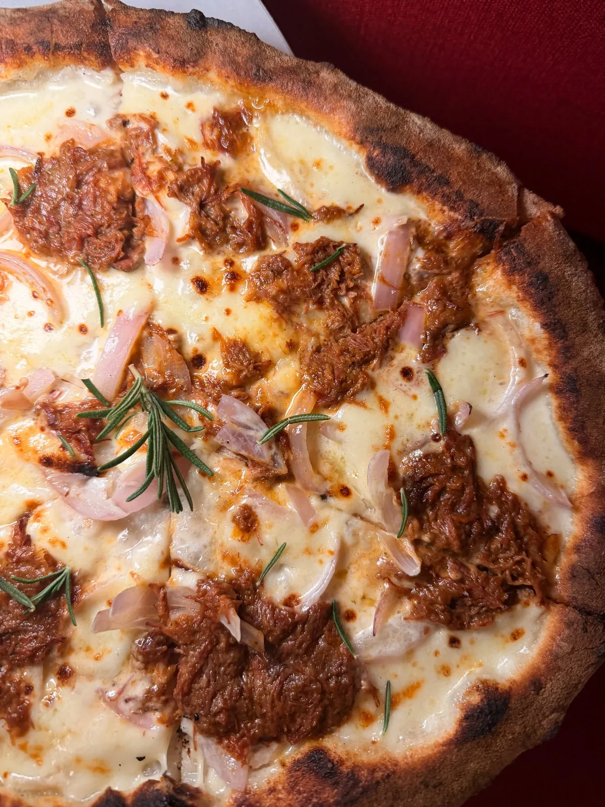 A white pizza with slow-cooked beef ragu, red onion and rosemary