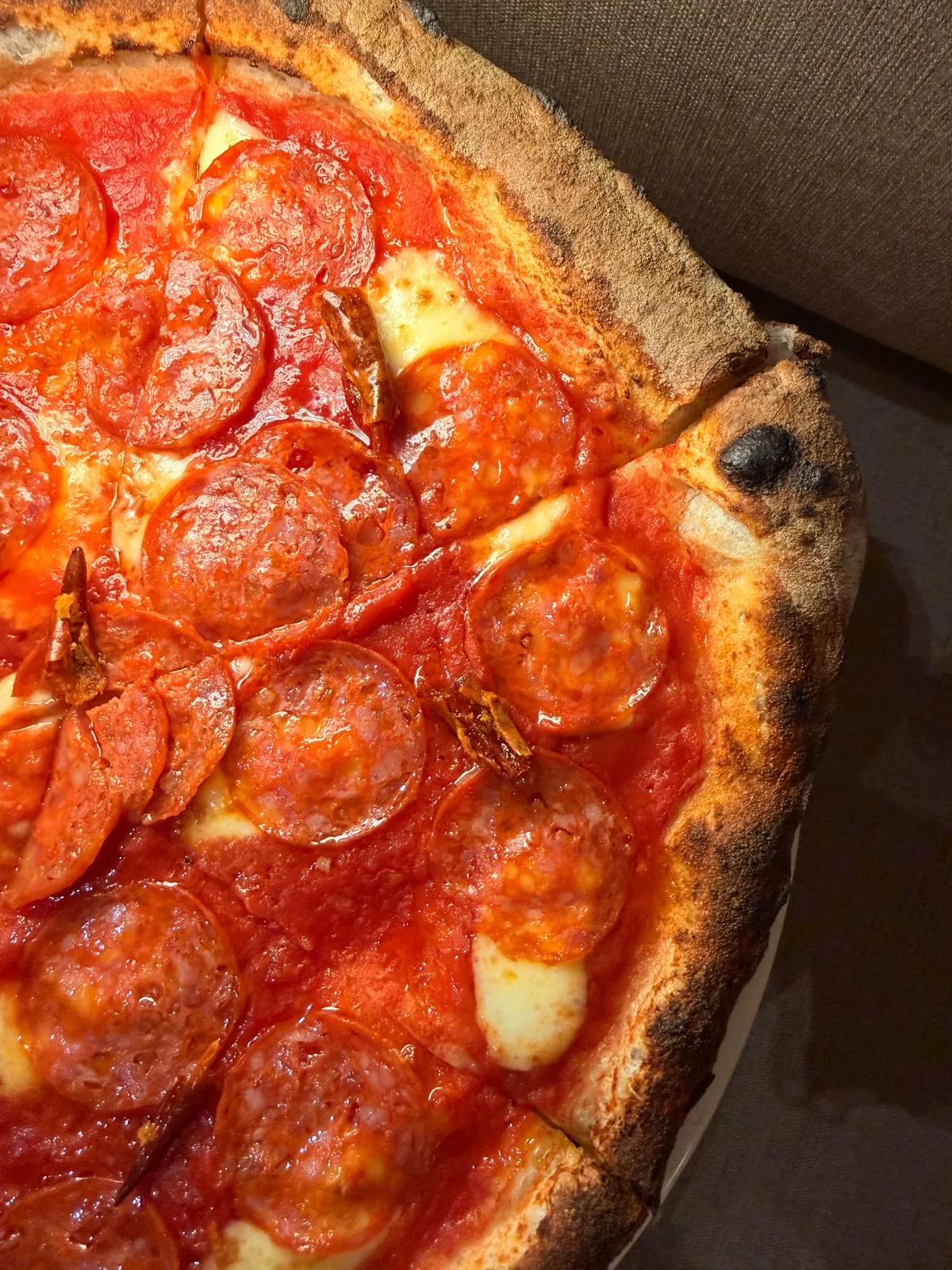 A pizza with rounds of spicy salami, tomato and mozzarella, scattered with dried chilli