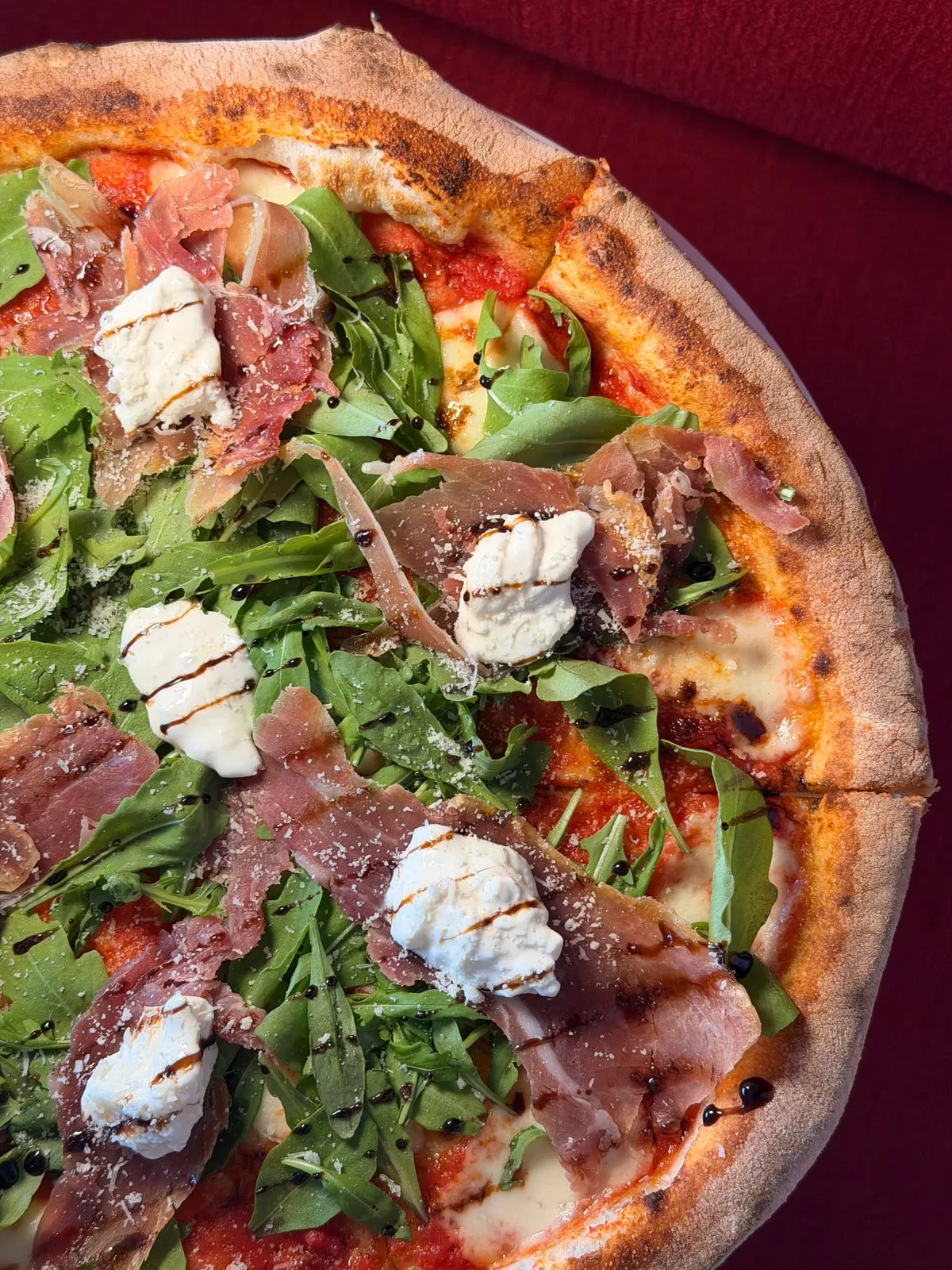 A pizza with prosciutto, wild rocket, stracciatella and balsamic