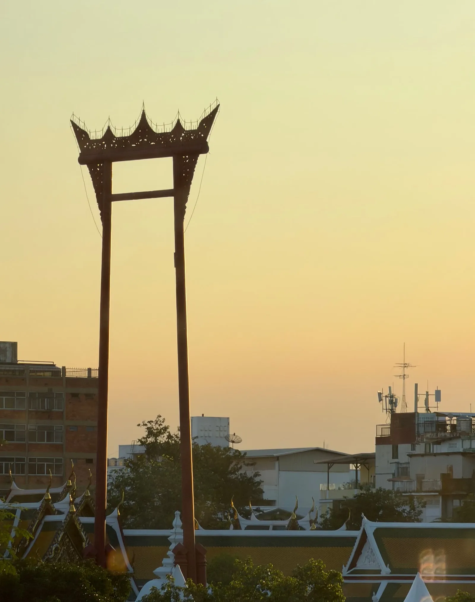 The Giant Swing standing above the temple roofs at sunset, seen from the end of Siri Phong Road