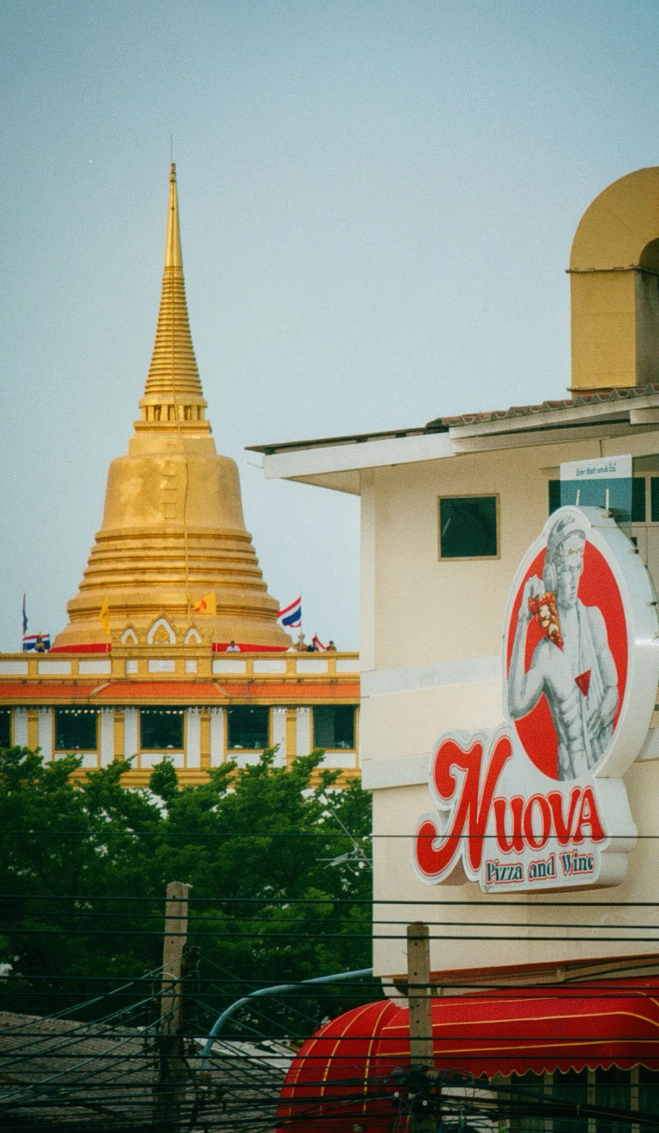 The Nuova sign on the shophouse wall, with the gold chedi of the Golden Mount rising behind it over the rooftops